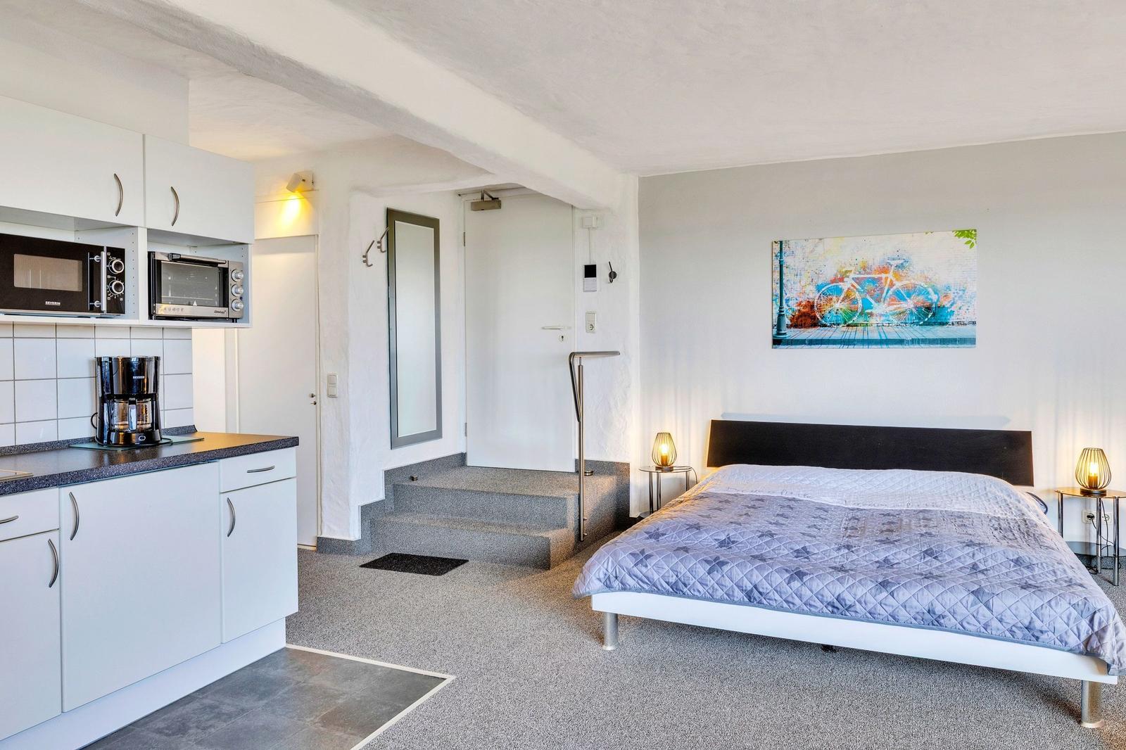 Schlafzimmer mit Bett, Küchenzeile und Wandbild mit Fahrrad.