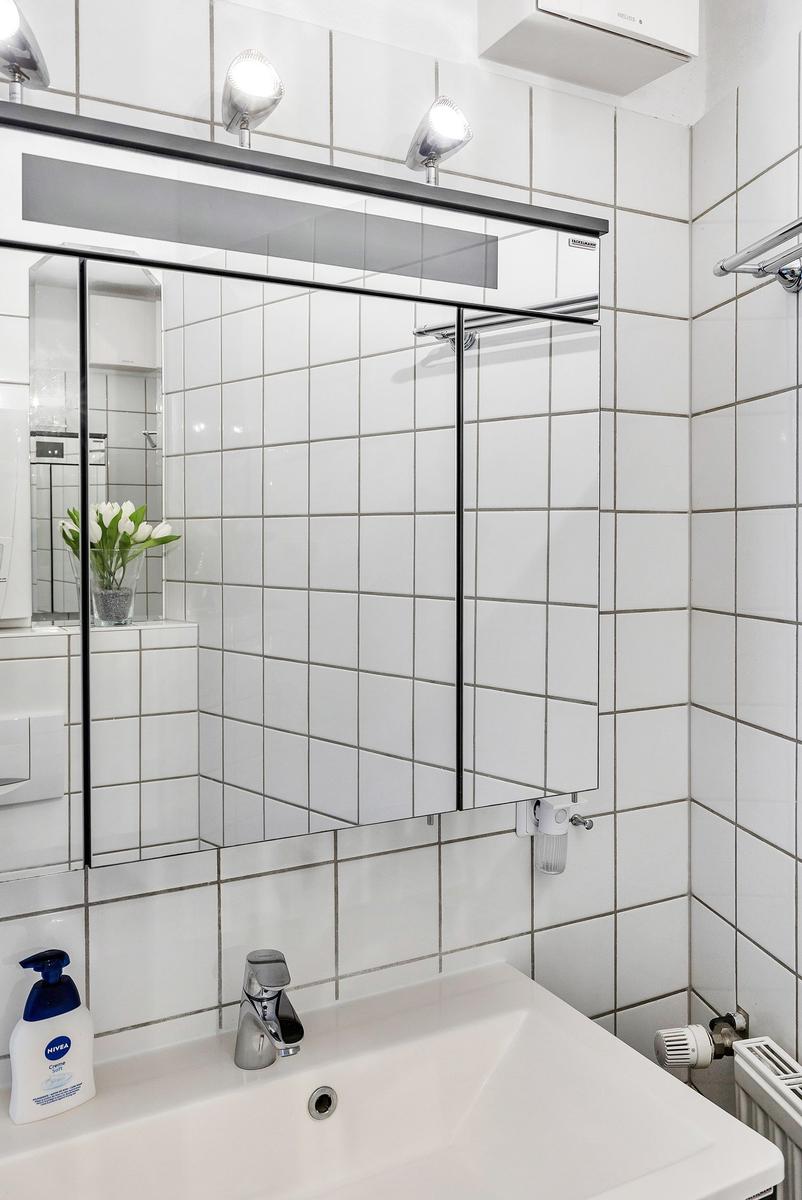 Badezimmer mit Spiegel, Waschbecken und weißen Fliesen.