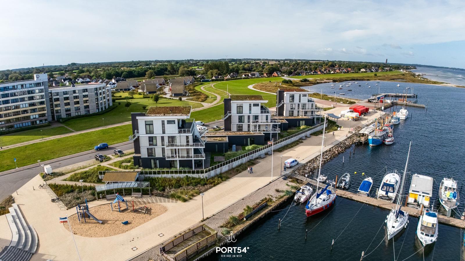 Hafen mit Booten, modernen Häusern und grünen Flächen am Wasser.