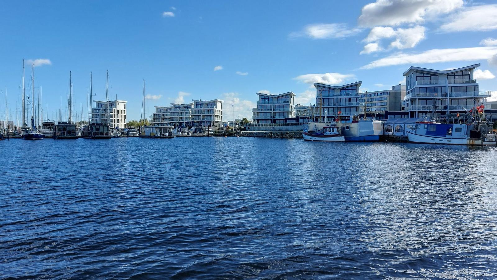 Hafen mit Booten und modernen Gebäuden am Wasser.