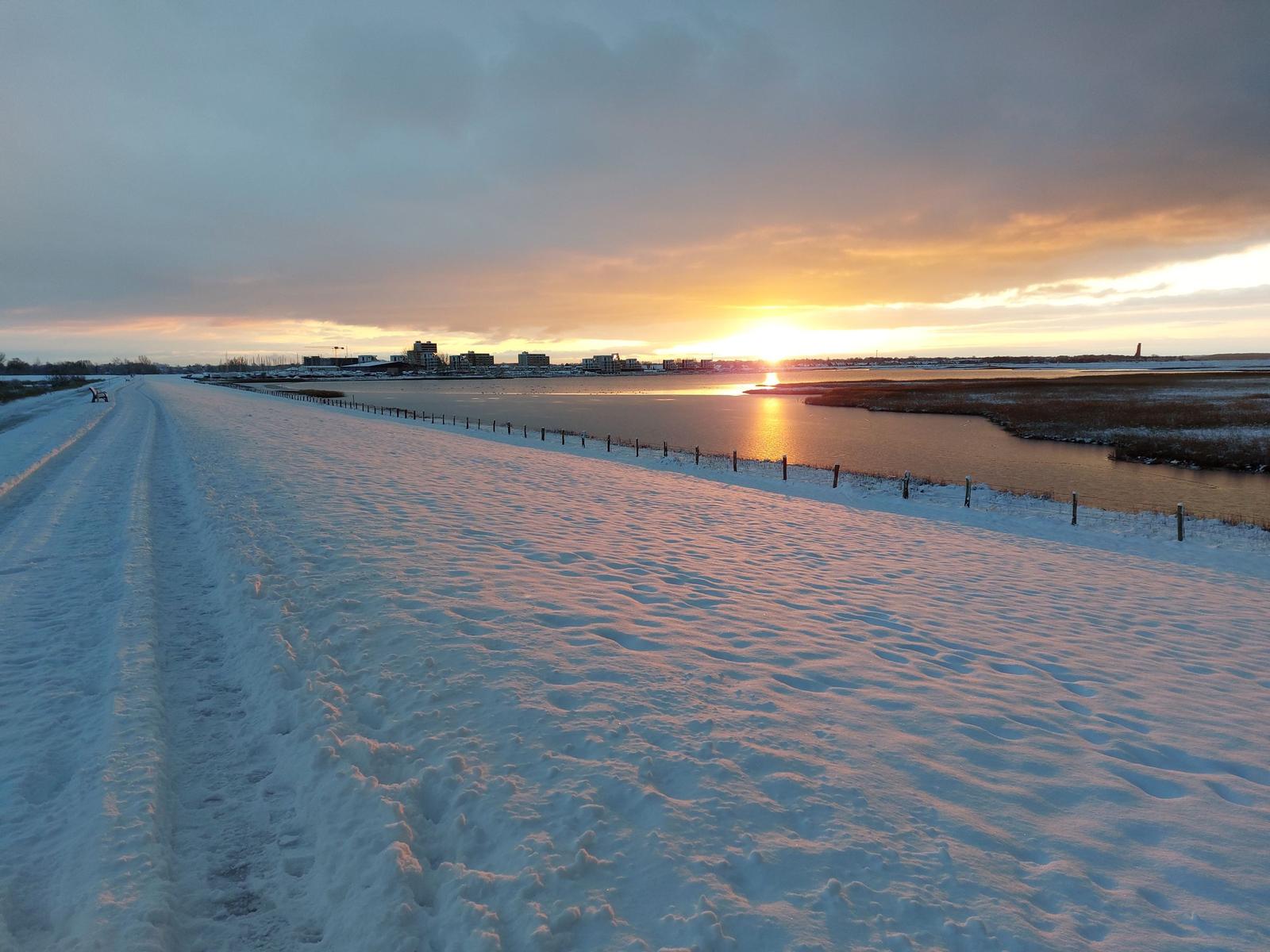 Schneebedeckter Weg entlang eines gefrorenen Sees bei Sonnenuntergang.