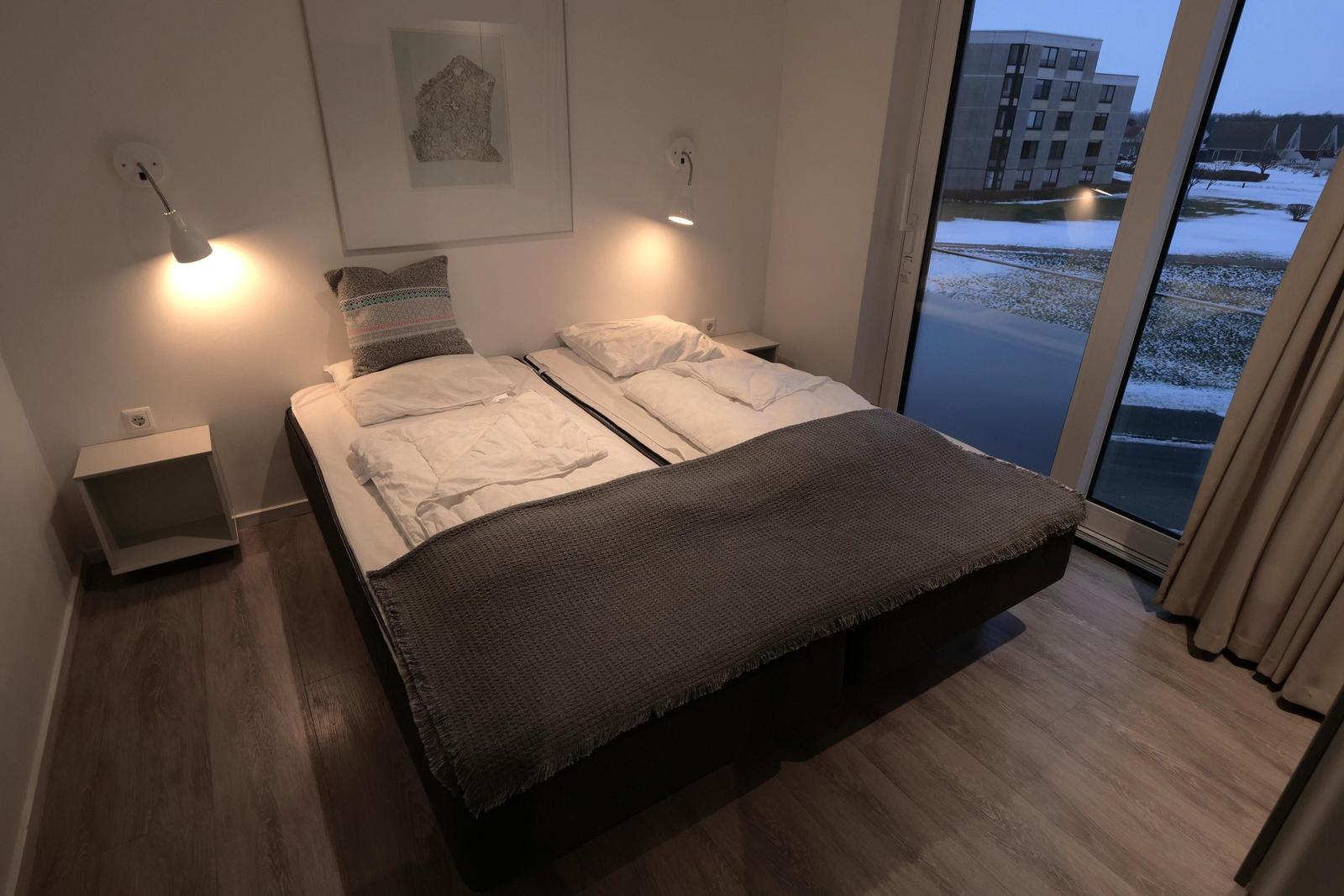 Schlafzimmer mit Doppelbett, großen Fenster und moderner Beleuchtung.
