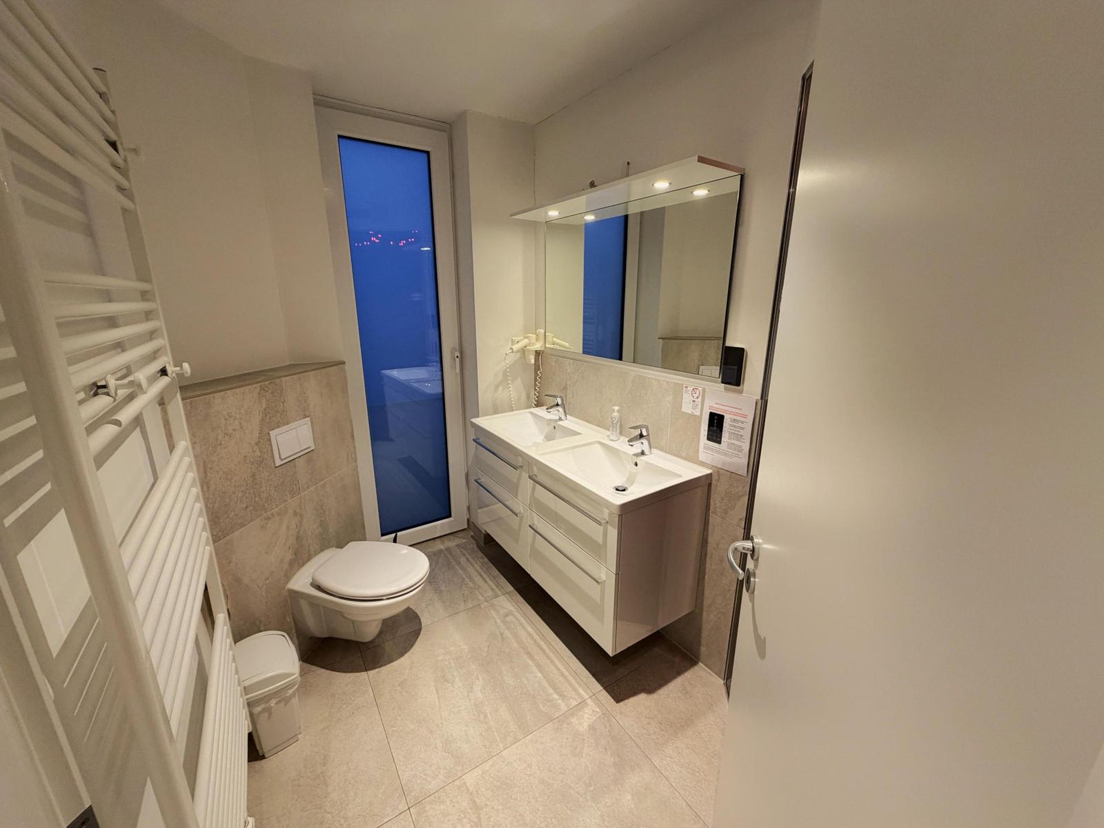 Badezimmer mit Doppelwaschbecken, Toilette und Heizkörper