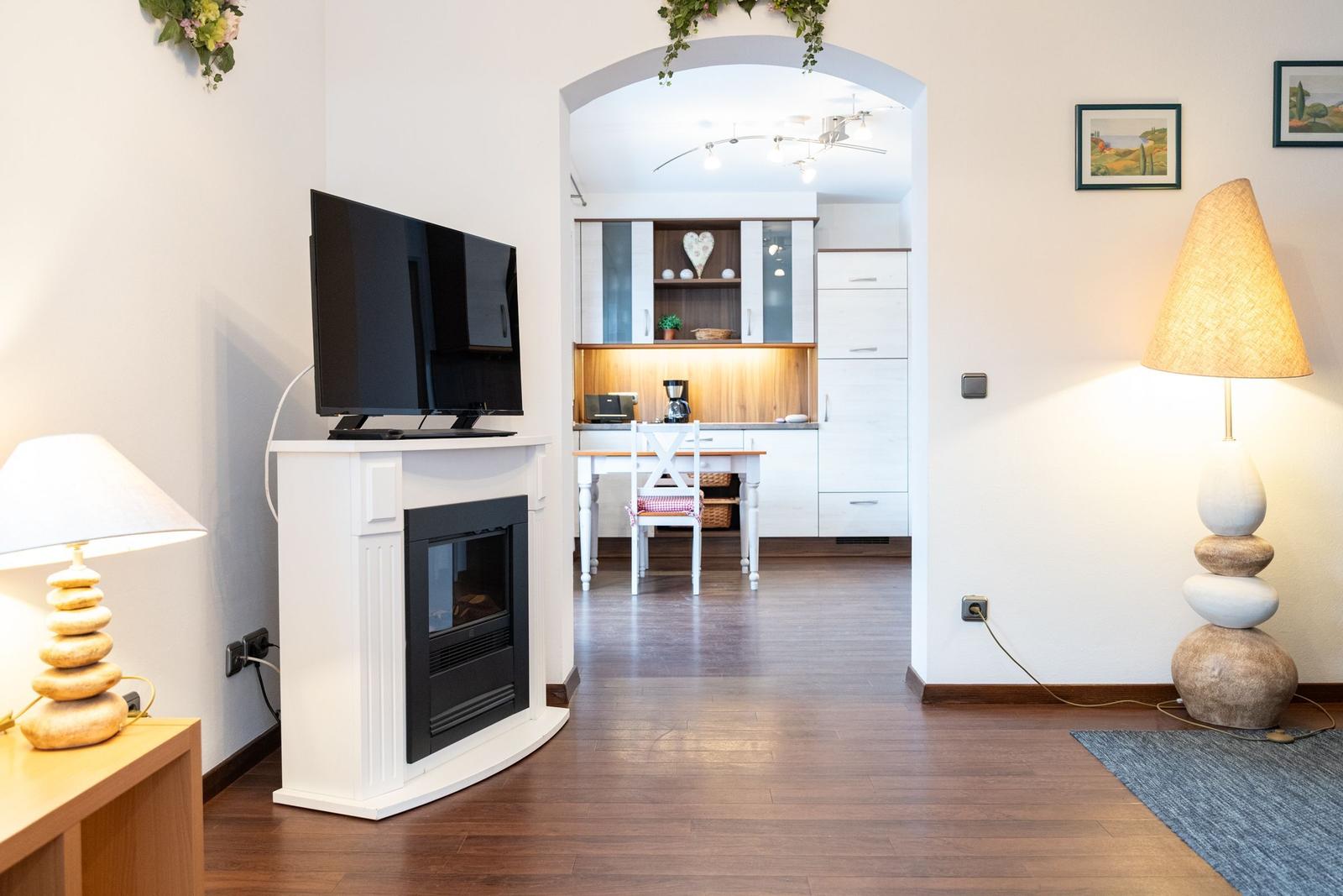 Wohnbereich mit Fernseher und Kamin, Blick in die Küche mit Esstisch.