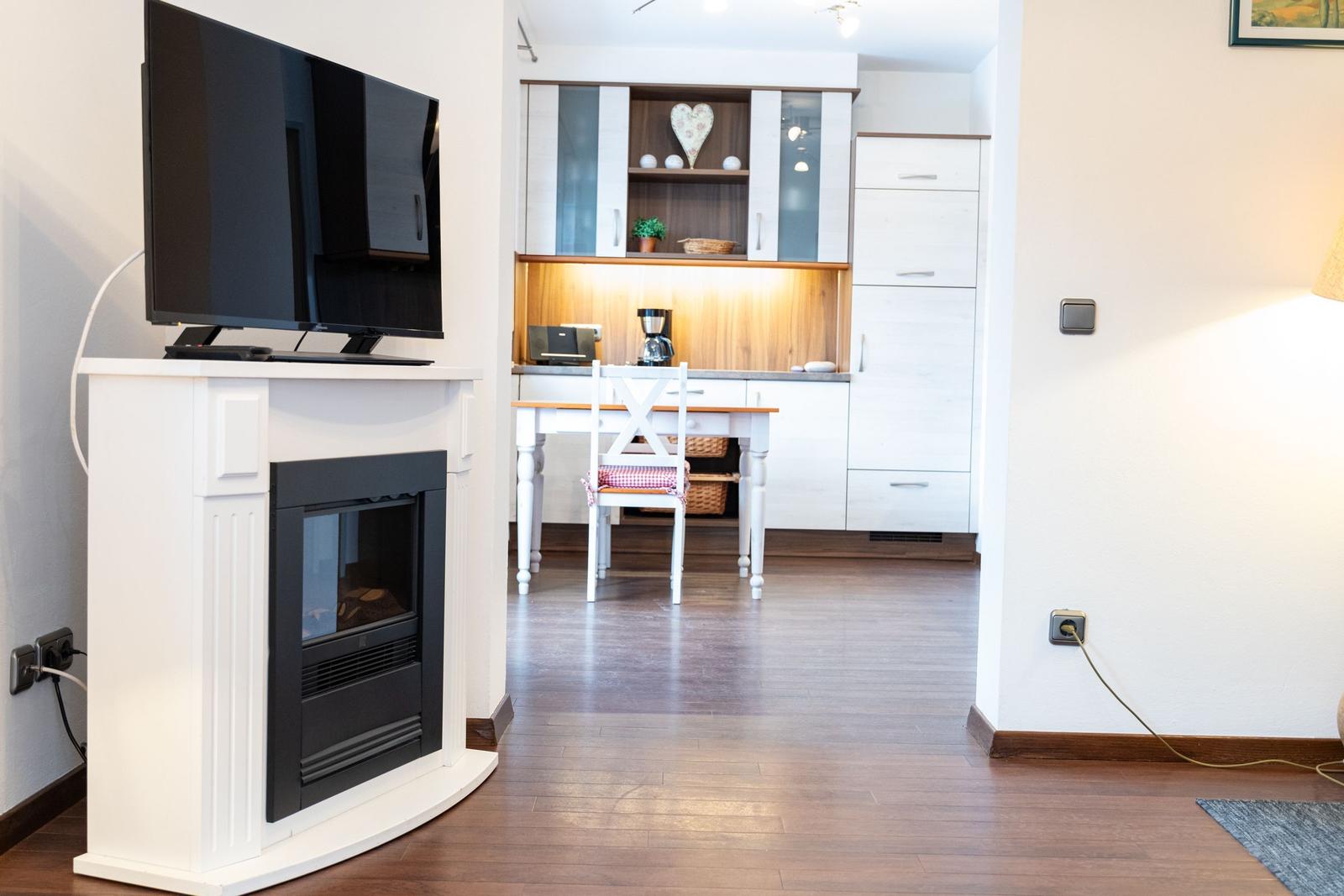 Wohnbereich mit Kamin und TV, Küche mit Esstisch und Küchenschränken.