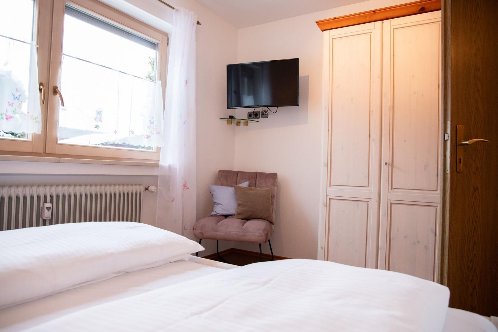 Schlafzimmer mit Bett, Fenster, Kleiderschrank und TV.