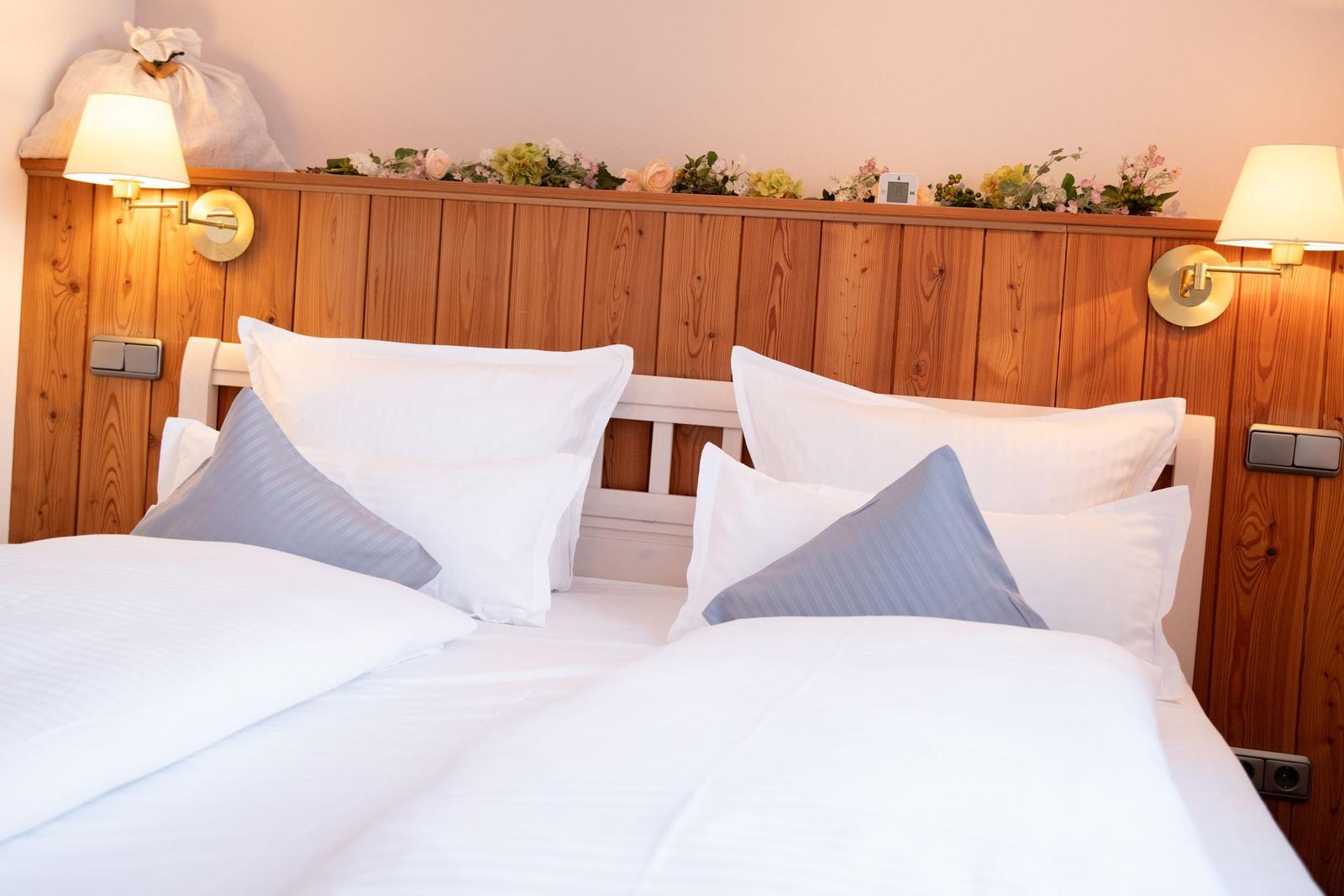 Doppelbett mit weißen Bettwäsche und grauen Kissen. Holzpaneelen und Wandlampen.