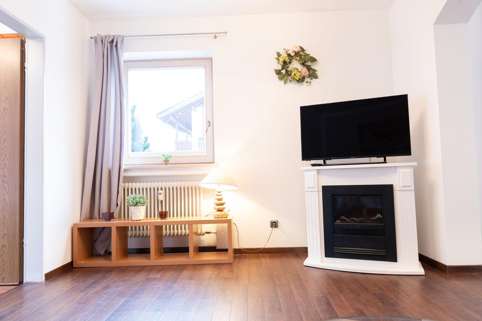 Wohnzimmer mit Fernseher, Kamin und Fenster mit Vorhang.