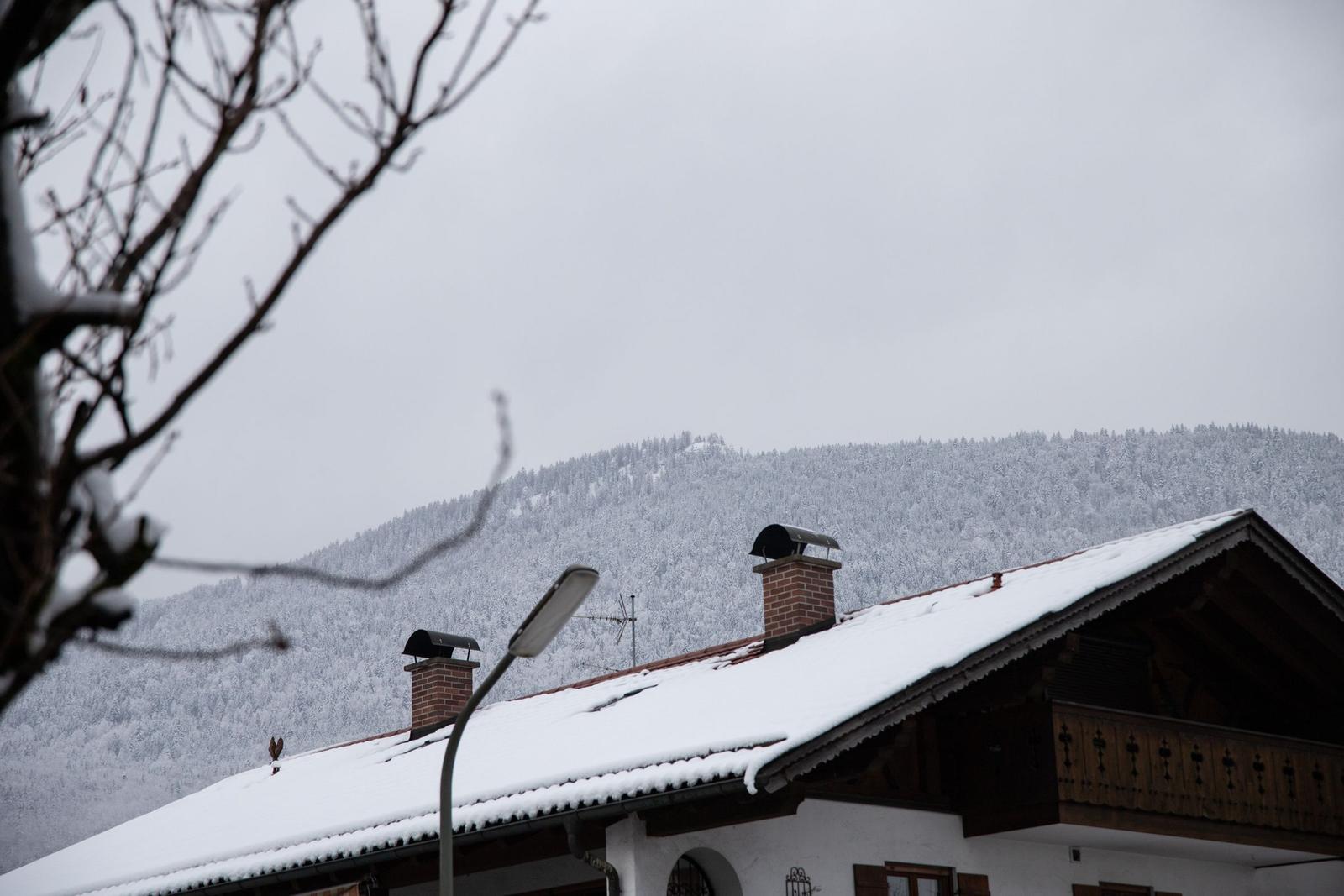 Schneebedecktes Dach mit Schornsteinen und verschneiten Bergen im Hintergrund.