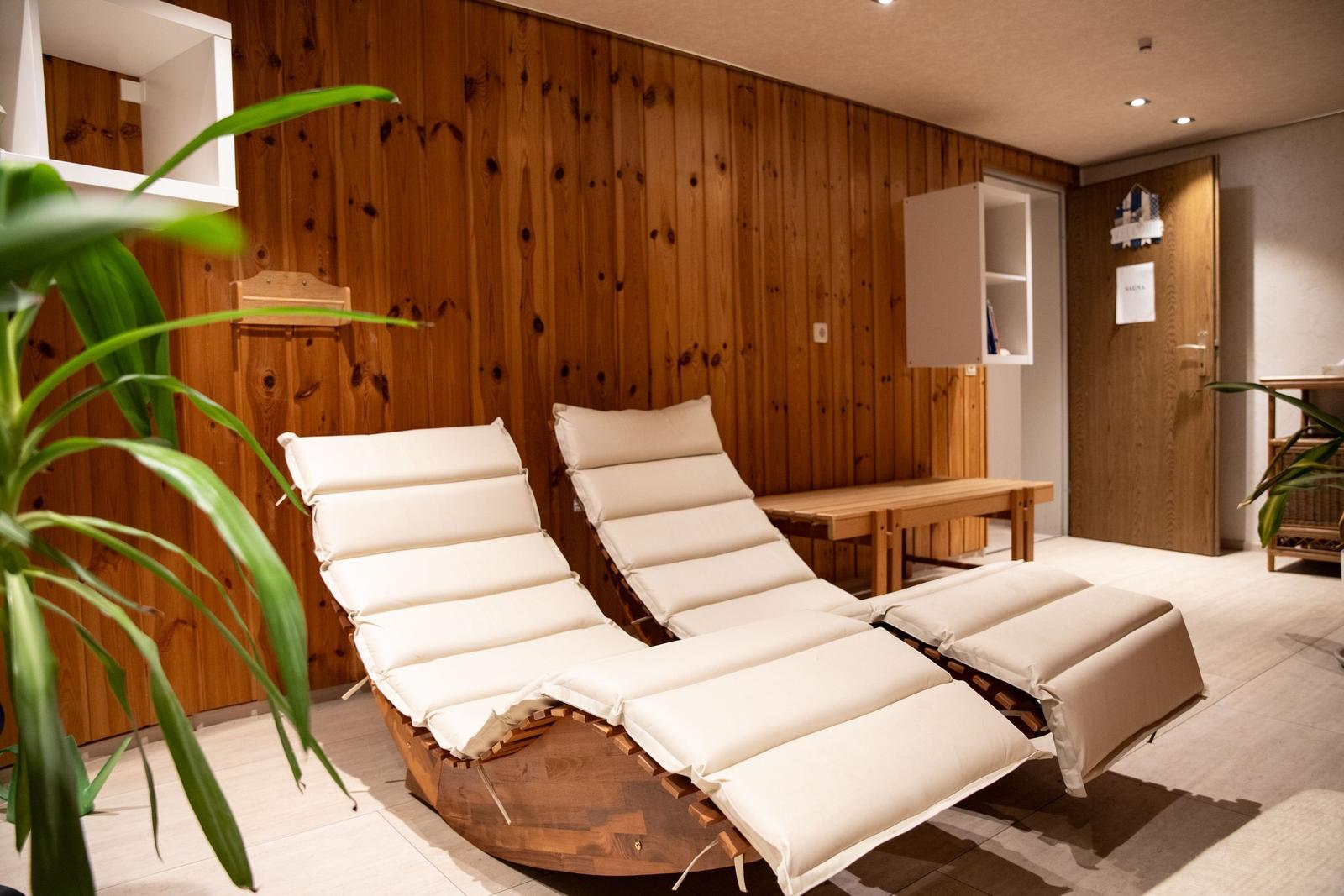 Zwei Liegestühle mit Kissen stehen in einem Raum mit Holzwand und Pflanzen.