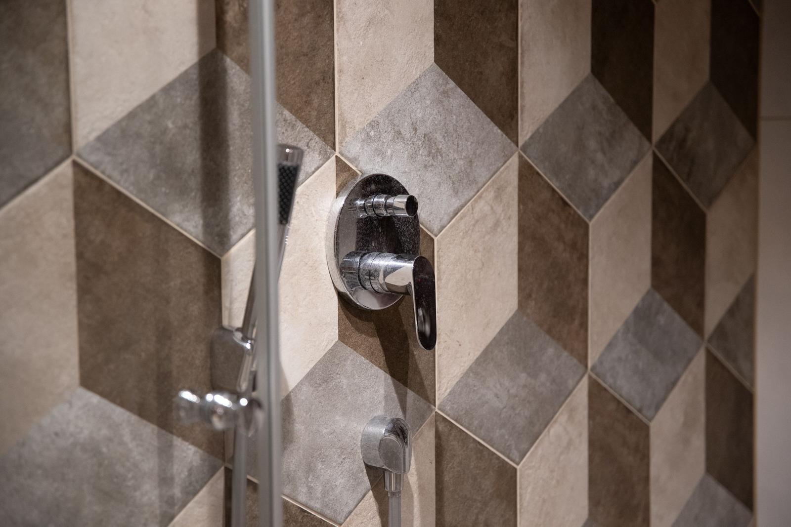 Dusche mit Chromarmatur und geometrischem Fliesenmuster in Braun- und Grautönen.