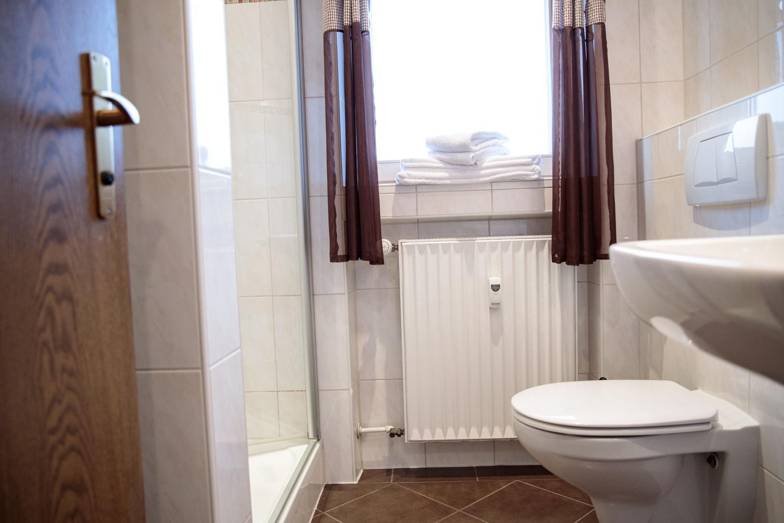 Badezimmer mit Dusche, Toilette und Waschbecken. Fenster mit Handtuchstapel.