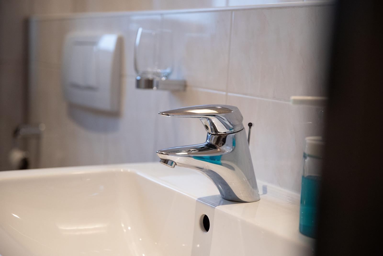 Waschbecken mit modernem Wasserhahn und blauem Seifenspender