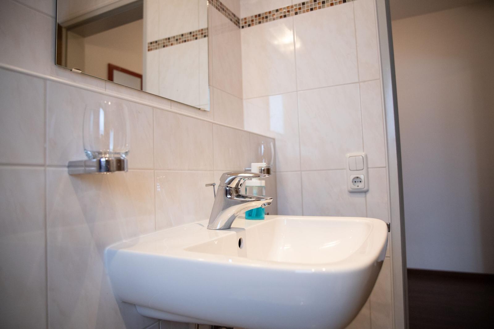 Waschbecken mit Spiegel und Flaschenhalter an der Wand.