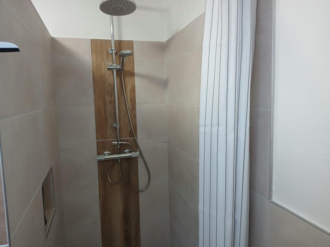 Shower with showerhead and handheld shower, beige tiles and wood panel.