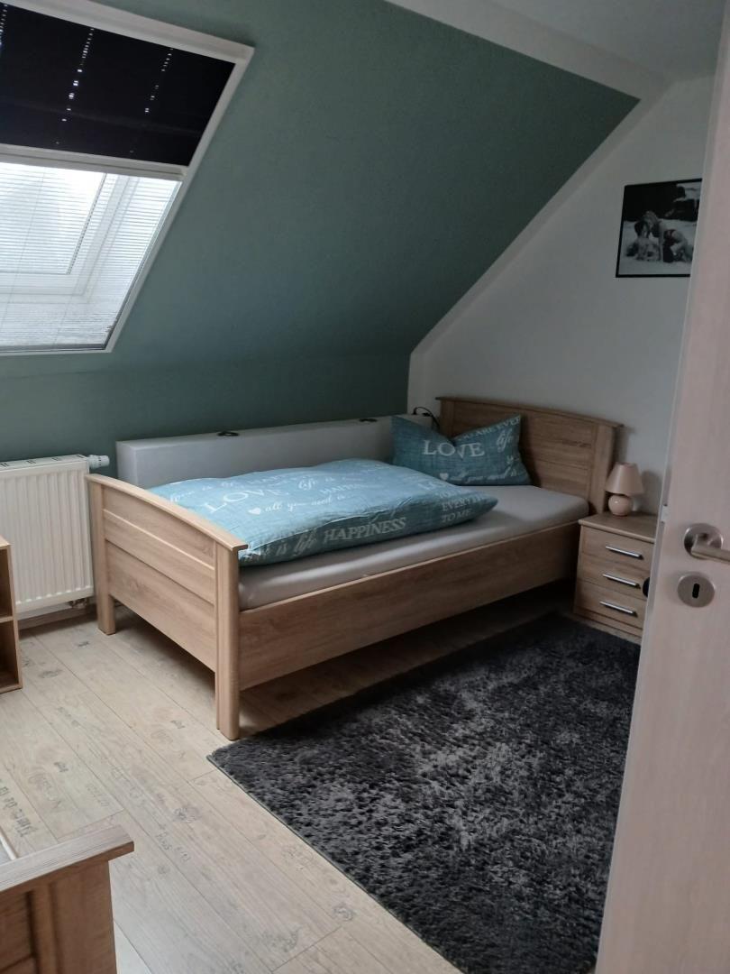 Bedroom with sloped ceiling, wooden bed, window, and nightstand.
