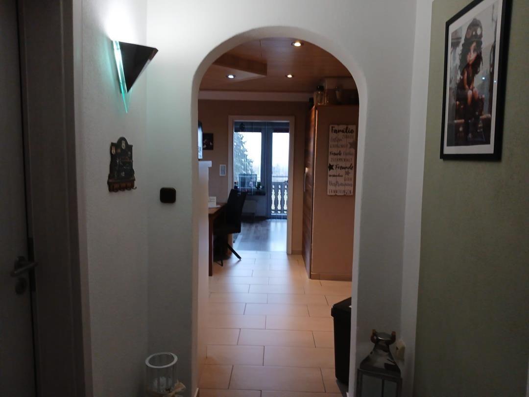 Hallway with arch leads to kitchen and dining area. Wall decor and floor tiles visible.