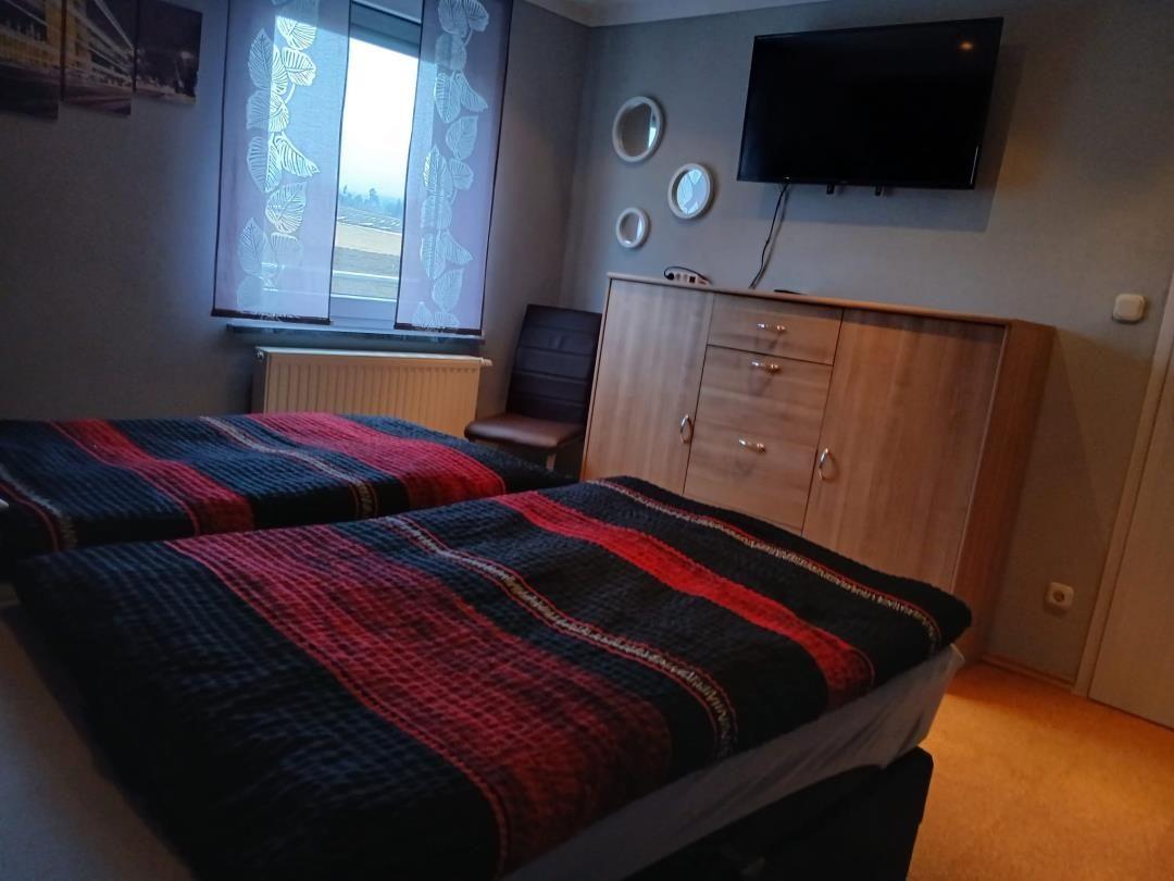 Two beds with striped bedcovers, wardrobe, and TV on the wall.