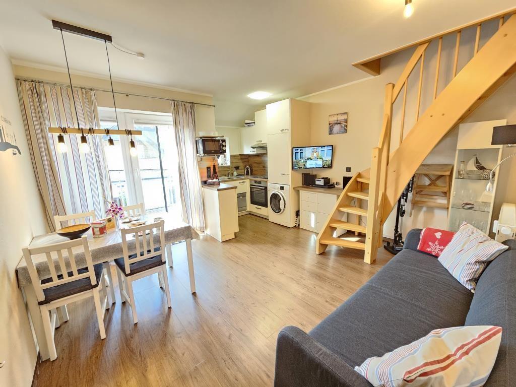 Living kitchen with dining area, sofa, and wooden staircase to upper level.
