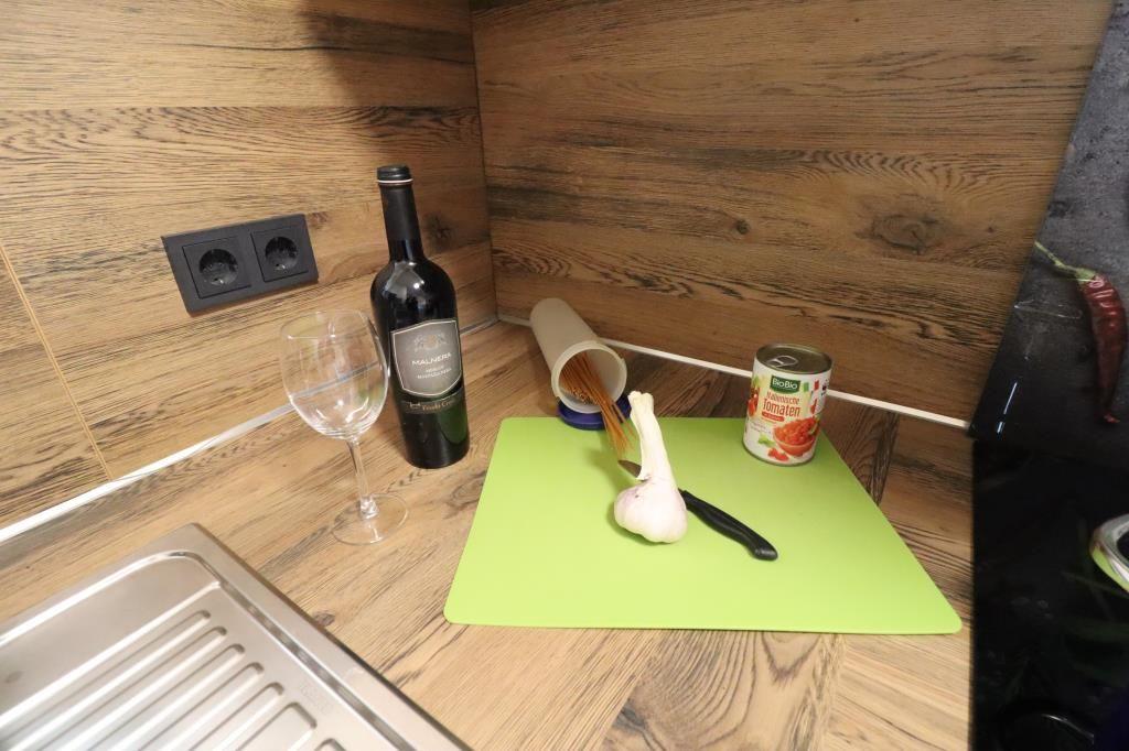 Kitchen area with wine bottle, spaghetti, garlic, and tomato can on green cutting board.