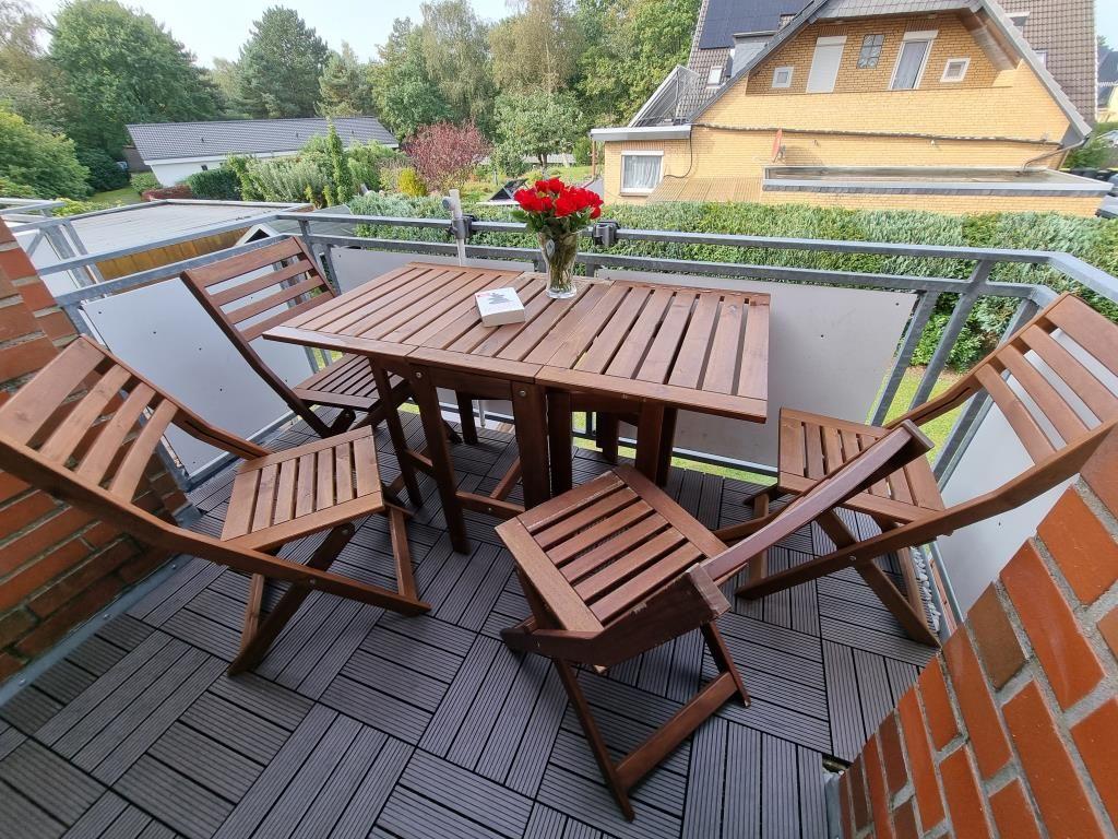 Terrace with wooden table and chairs, flowers, and view of garden and neighboring house.