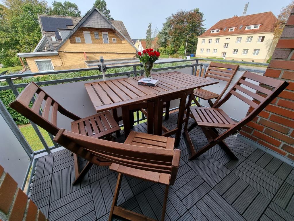 Terrace with wooden table and chairs, flowers, and view of houses.
