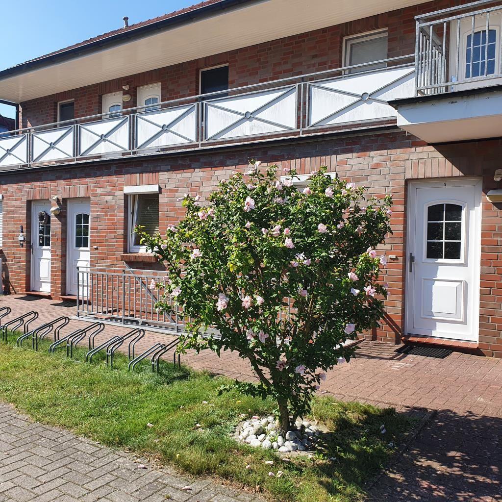 Two-story house with balconies, white doors, and flowering tree in front.