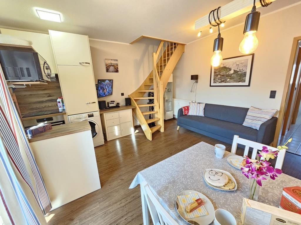 Living kitchen with dining area, sofa, and wooden staircase.