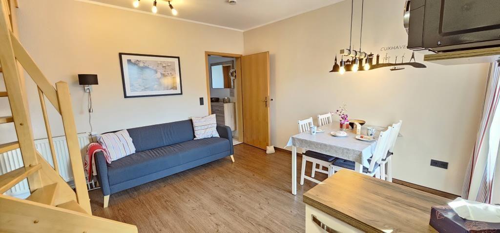 Living and dining area with sofa, table and chairs. Wooden floor and staircase visible.
