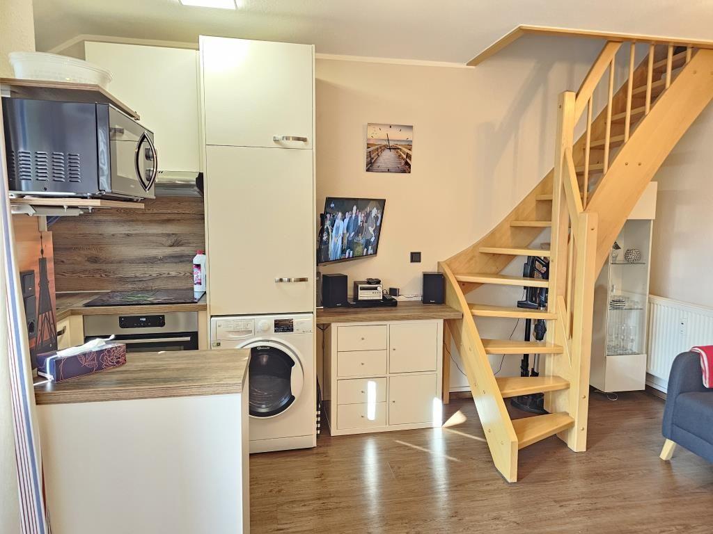 Kitchen with washing machine, TV, and wooden staircase to upper level.