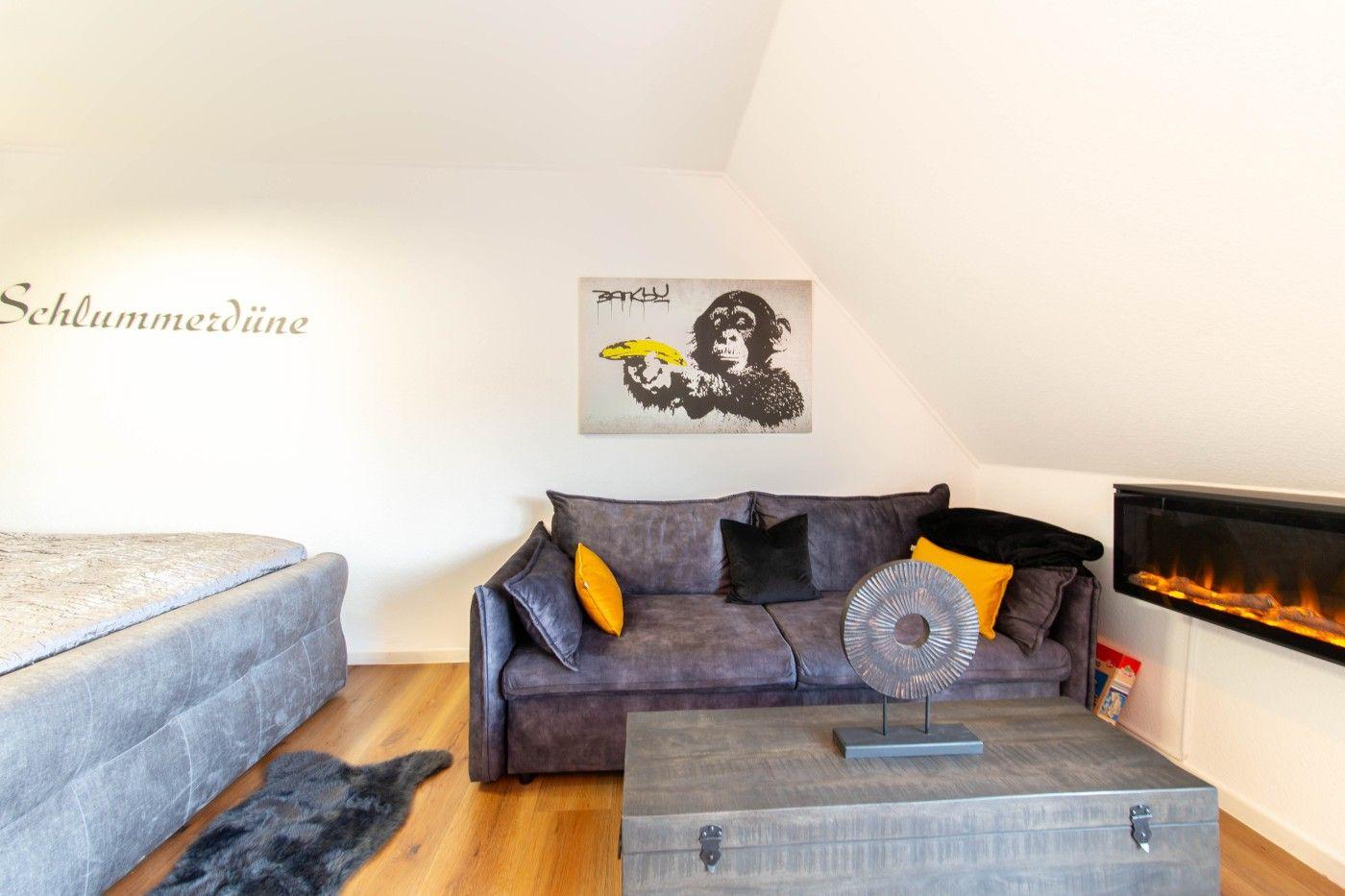 Schlafzimmer mit Sofa, Kamin und Wandbild. Bett links, Holzboden.