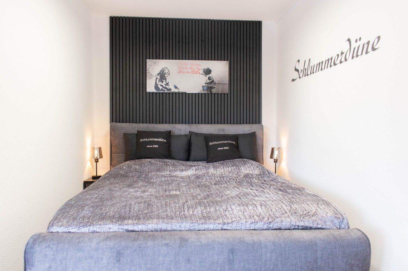 Schlafzimmer mit großem Bett, schwarzer Wand und Wandbild.