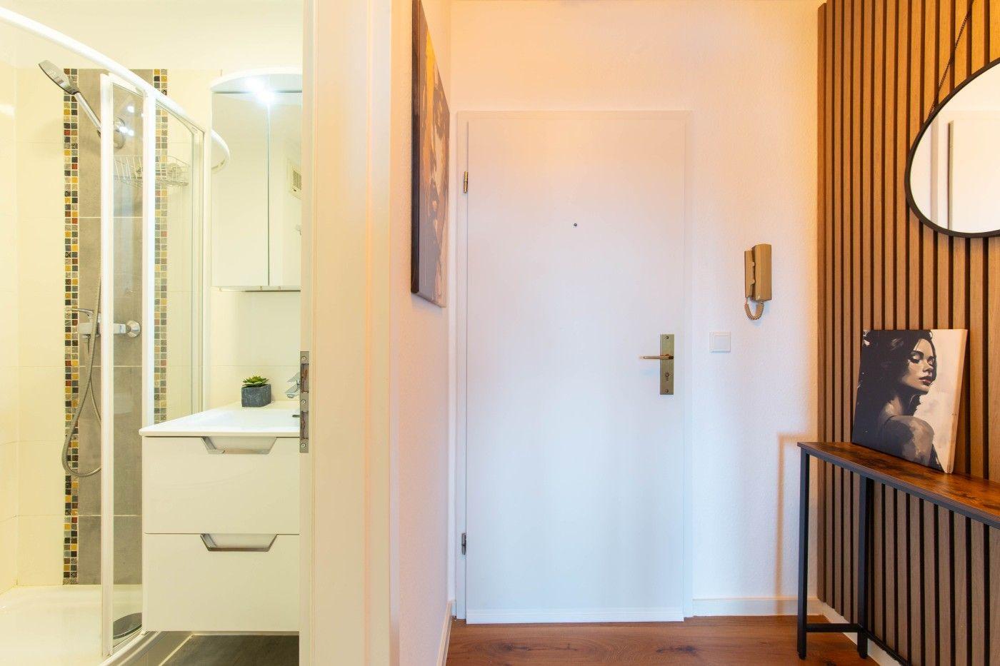 Eingangsbereich mit Tür, Spiegel und Badezimmer mit Dusche.