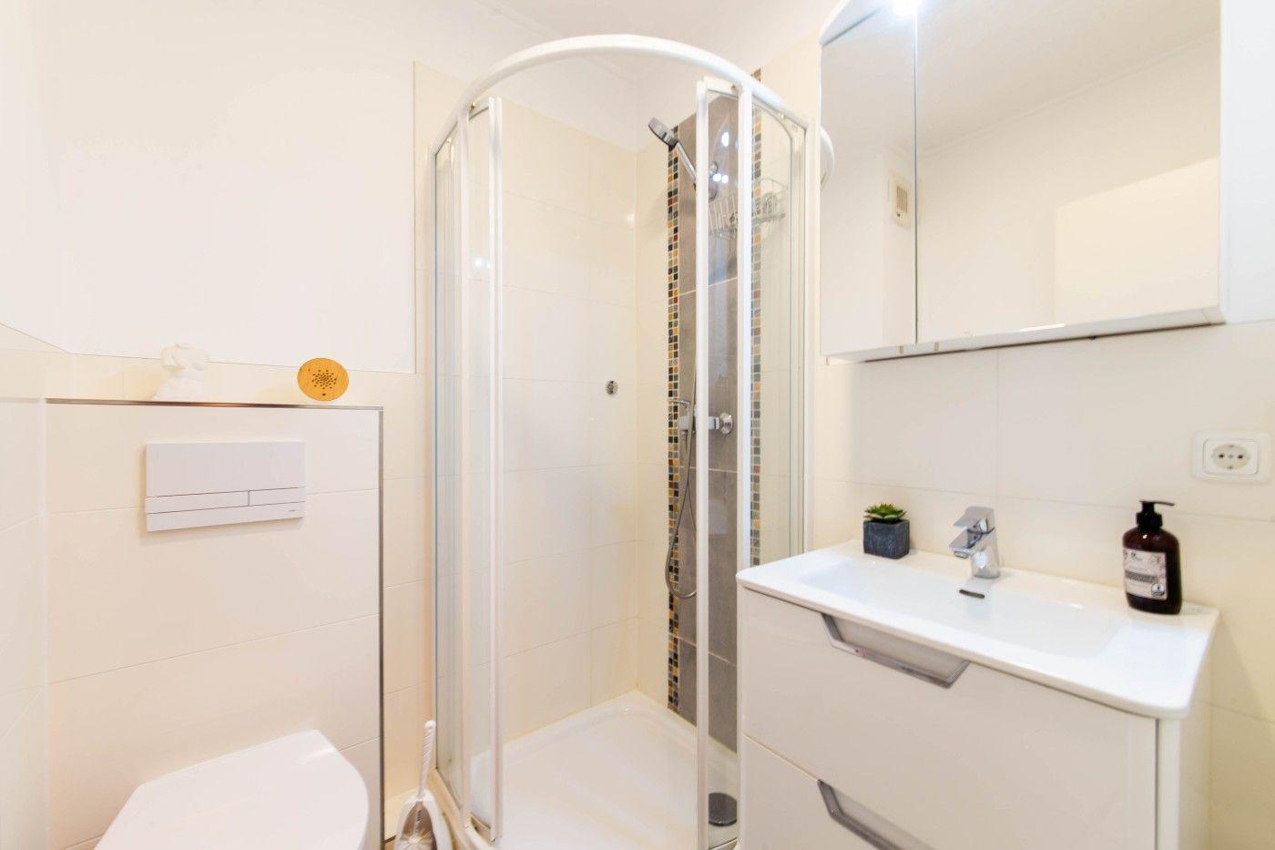 Badezimmer mit Dusche, Waschbecken und Toilette. Weiße Fliesen und Spiegelschrank.