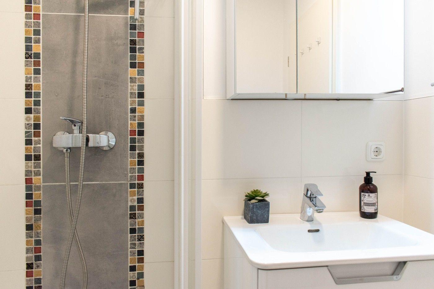 Badezimmer mit Dusche und Waschbecken. Mosaikfliesen an der Duschwand.