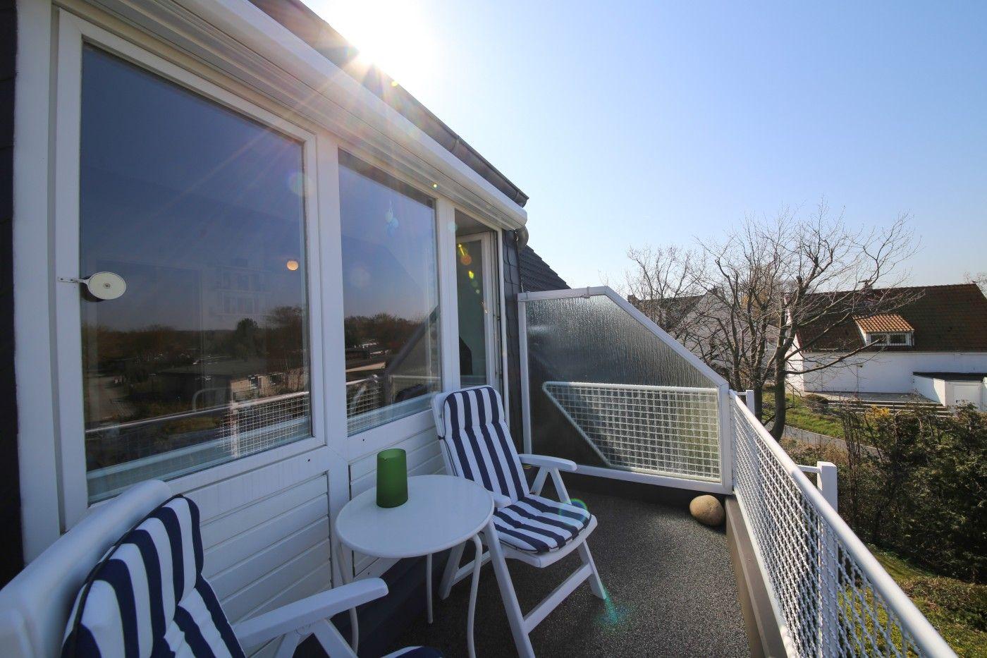 Terrasse mit zwei Stühlen und Tisch, weißer Geländer und Glaswand.