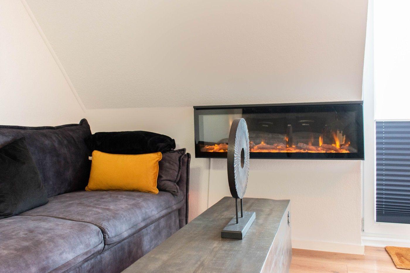 Ein Wohnzimmer mit grauem Sofa, gelbem Kissen und integriertem Kamin.