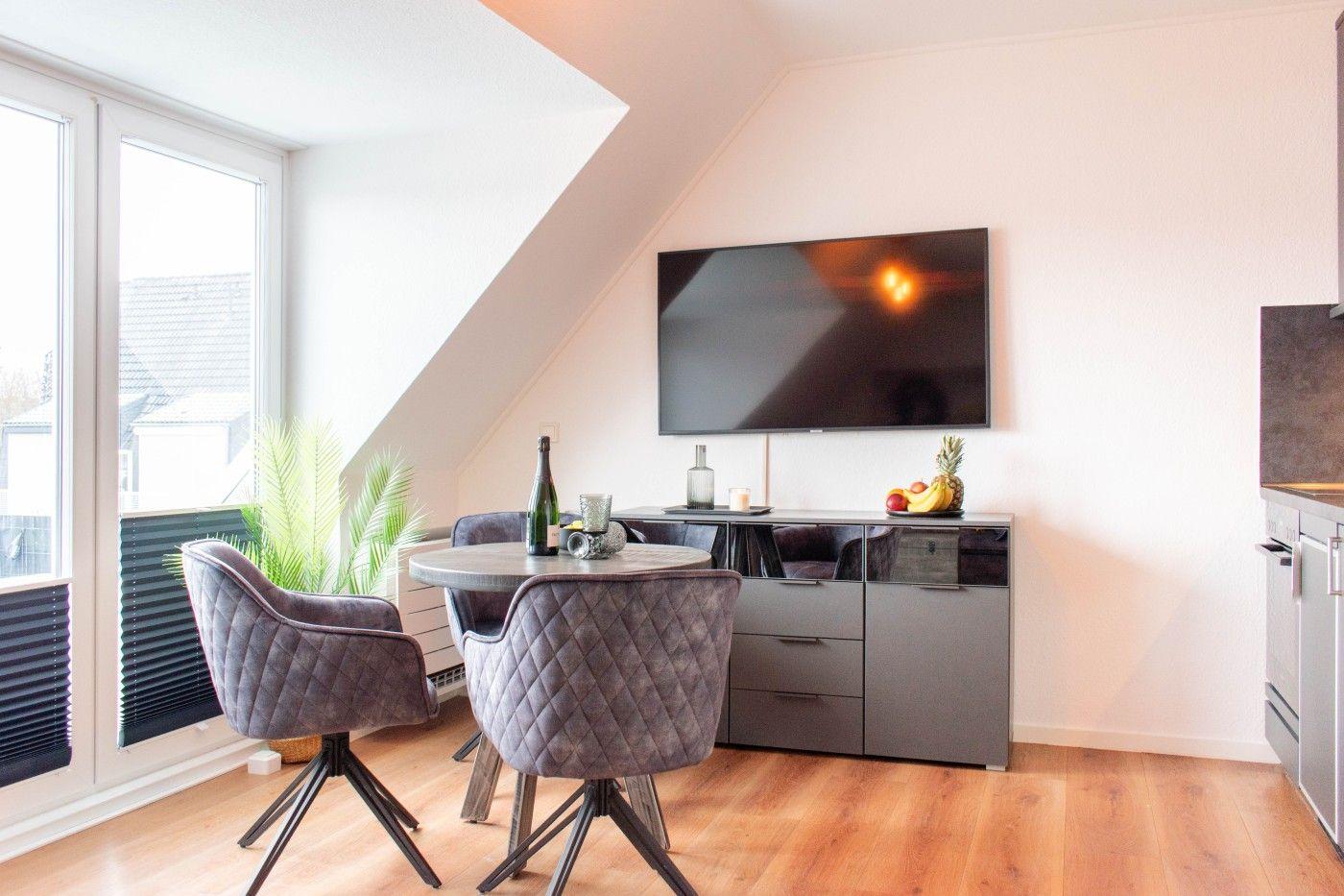 Dining area with round table, four chairs, TV, and large window.