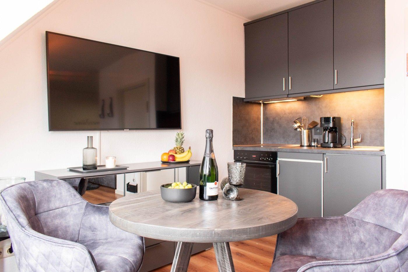 Küche und Essbereich mit runden Tisch, zwei Stühlen und Fernseher an der Wand.