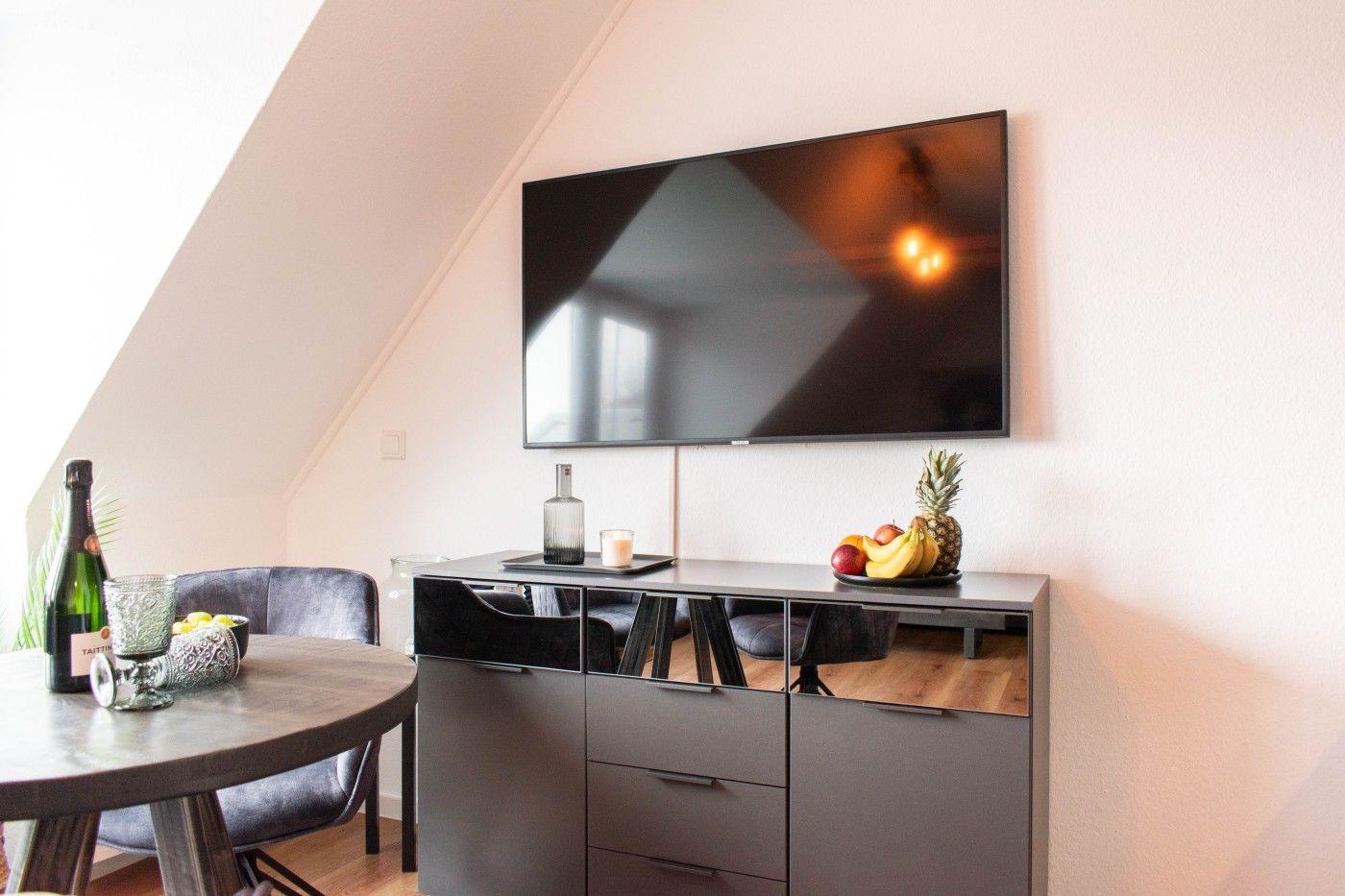 TV an der Wand, Schrank mit Obst und Flasche, Sitzgelegenheit im Dachgeschoss.