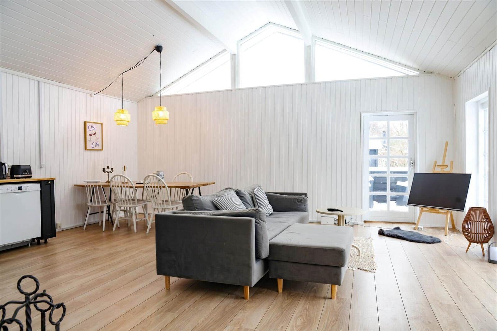 Wohn- und Essbereich mit Sofa, Tisch und Stühlen, Fernseher und Fenster.