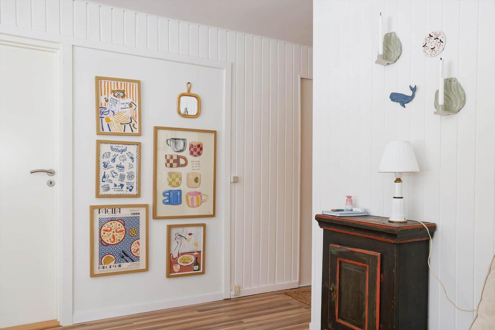 Wand mit Bildern und Dekorationen neben einem dunklen Schrank mit Lampe.