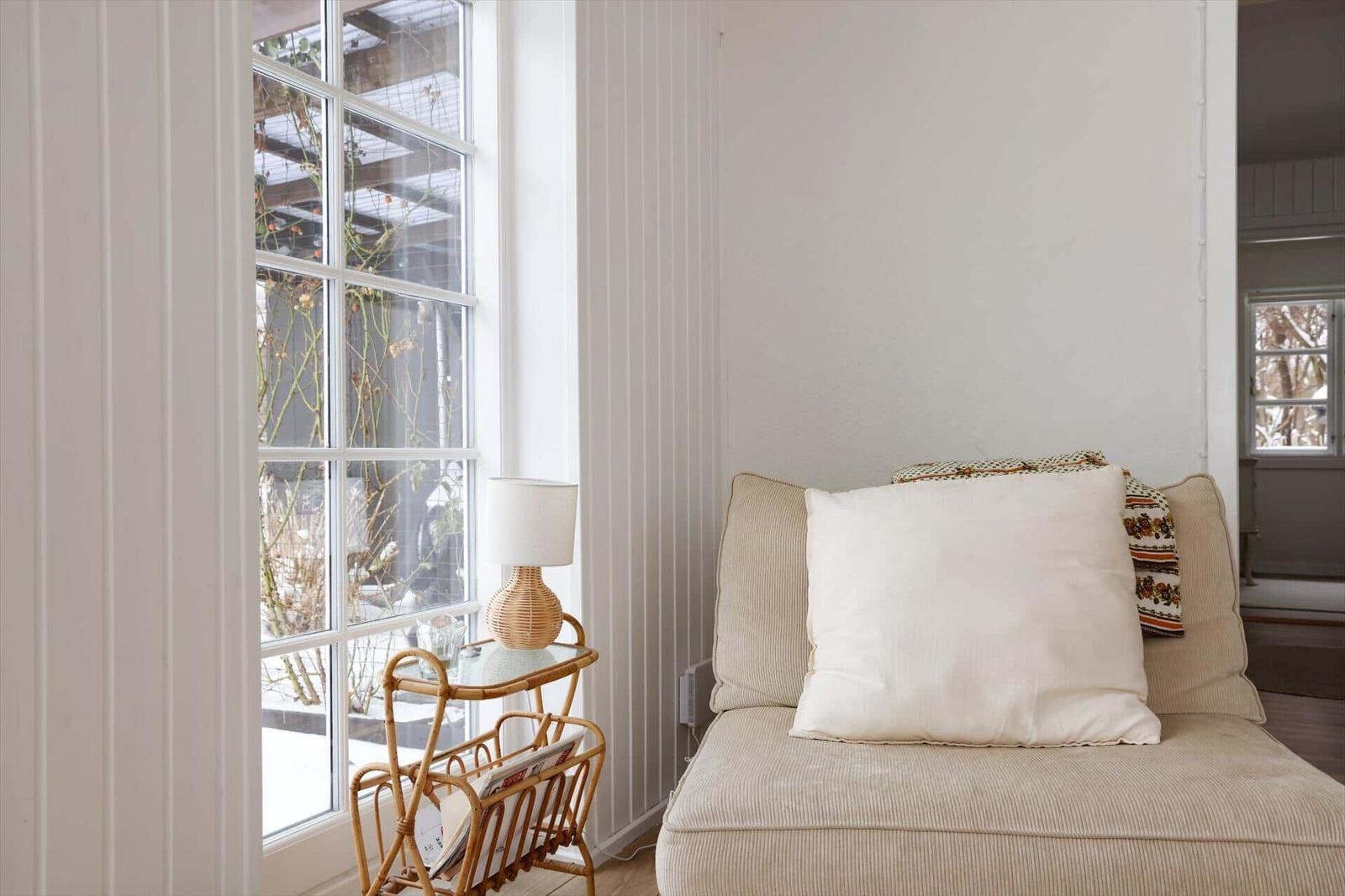 Ein Sofa mit Kissen steht neben einem Fenster mit Rattanbeistelltisch.