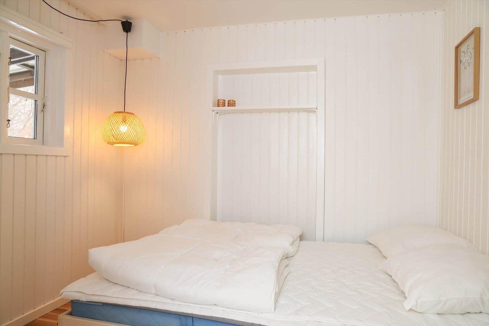 Schlafzimmer mit weißem Bett, Wandlampe und Fenster.