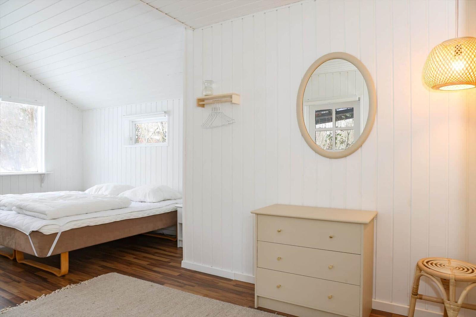 Schlafzimmer mit Bett, Schrank und Spiegel an weiß verputzten Wänden.