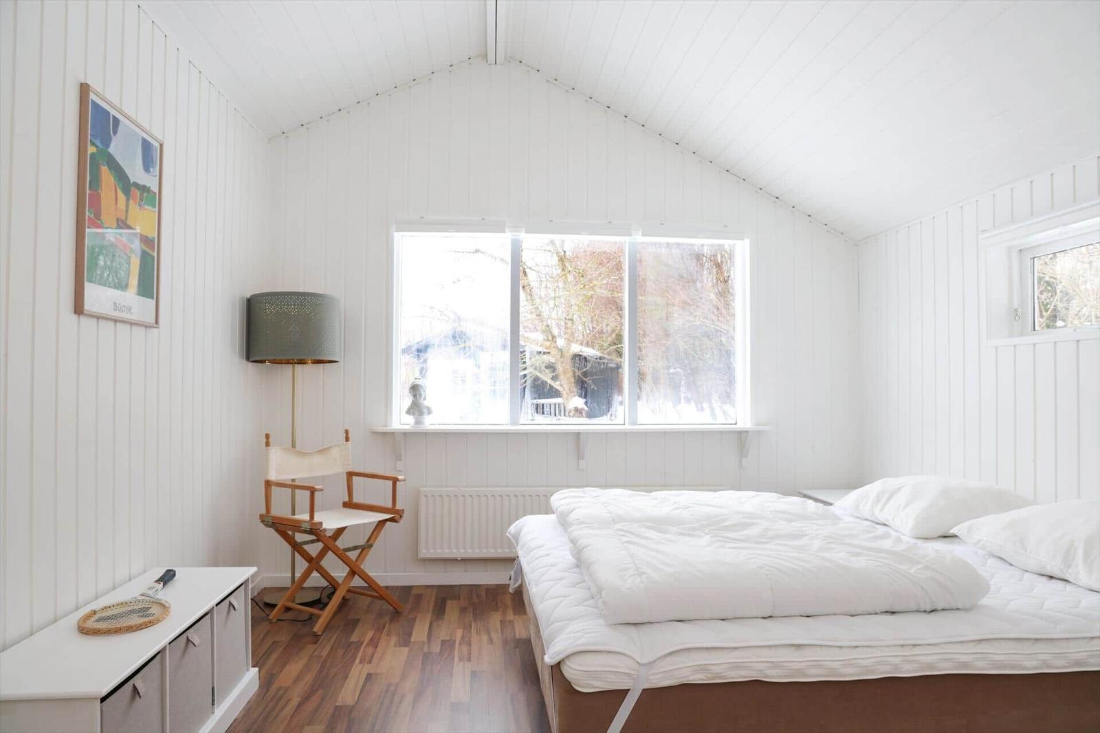 Schlafzimmer mit weißem Bett, Holzboden und großem Fenster.