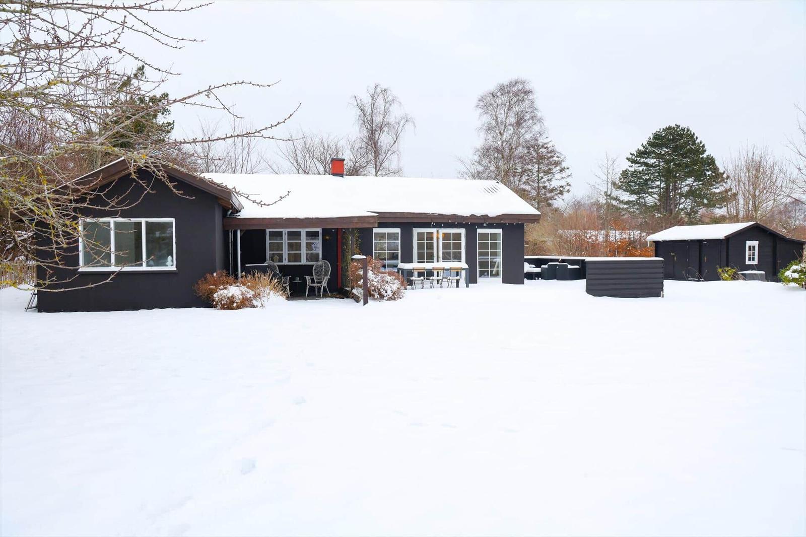Schwarzes Haus mit Schneebedecktem Dach und Gartenmöbeln im Winter.