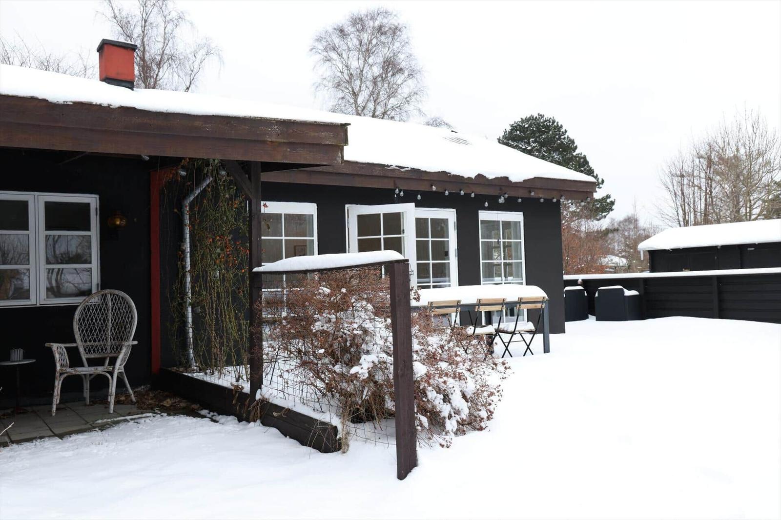 Schwarzes Haus mit Schnee, weißen Fenstern und Gartenmöbeln.