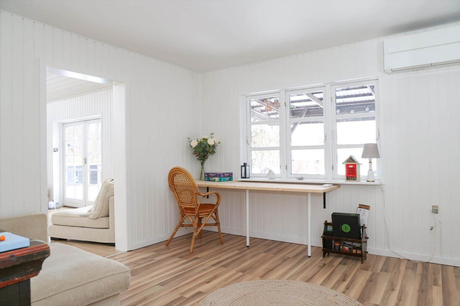 Ein Arbeitsbereich mit Schreibtisch, Stuhl und Fenster. Holzboden und weiße Wände.