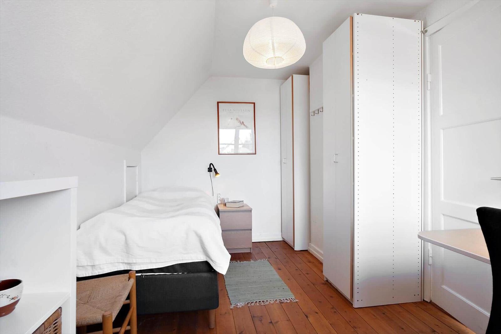 Bedroom with bed, wardrobe, and desk on wooden floor.